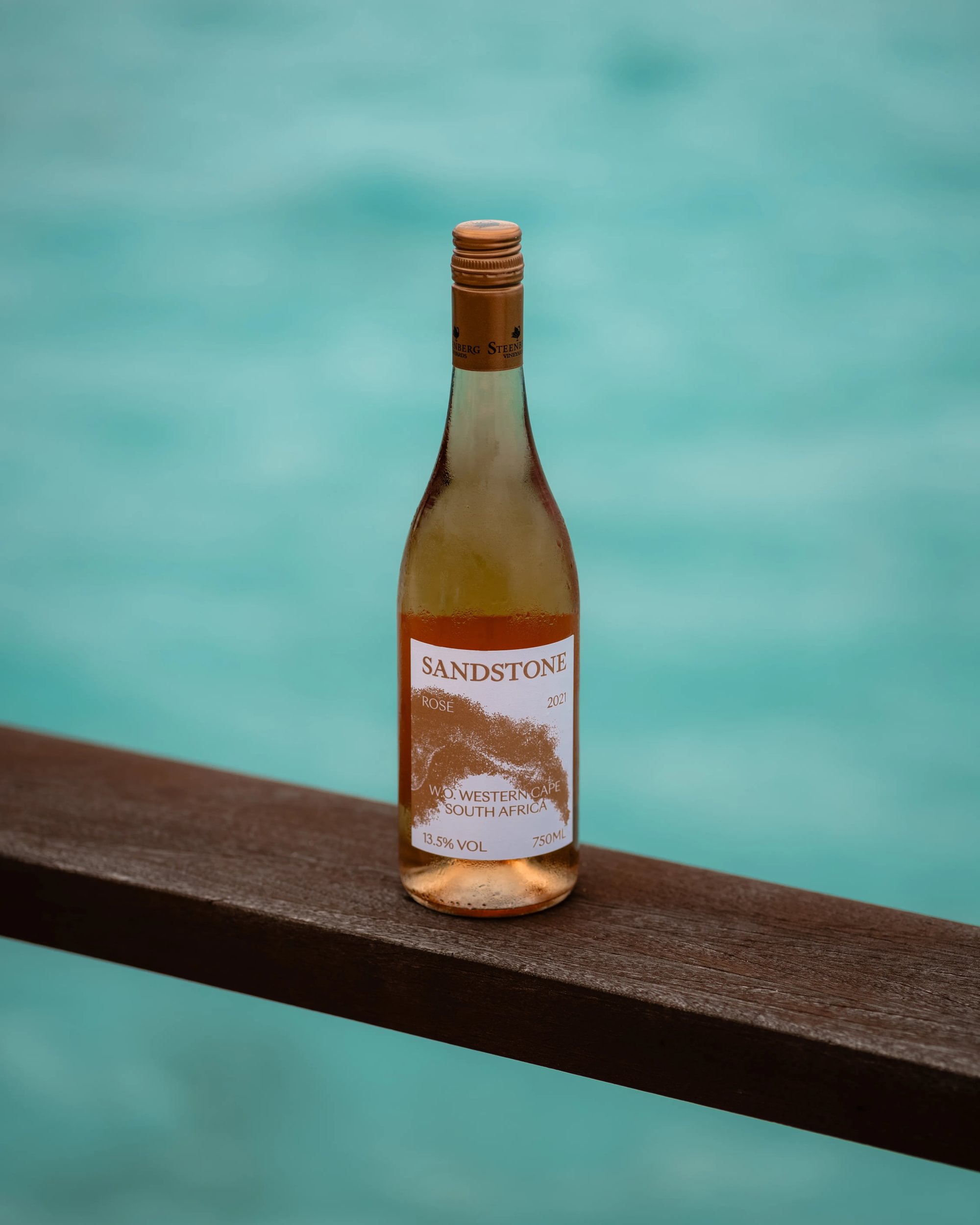 Bottle of Sandstone rosé at Villa Resorts placed on a wooden railing overlooking turquoise water