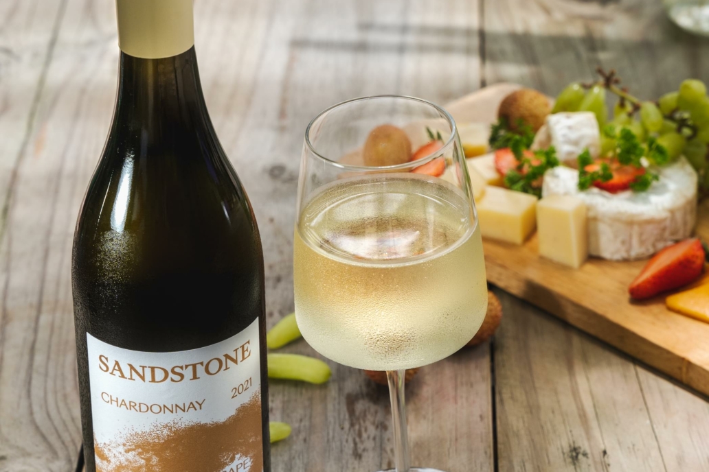 Bottle of Sandstone Chardonnay with a filled glass at Villa Resorts, set beside light dishes on a table