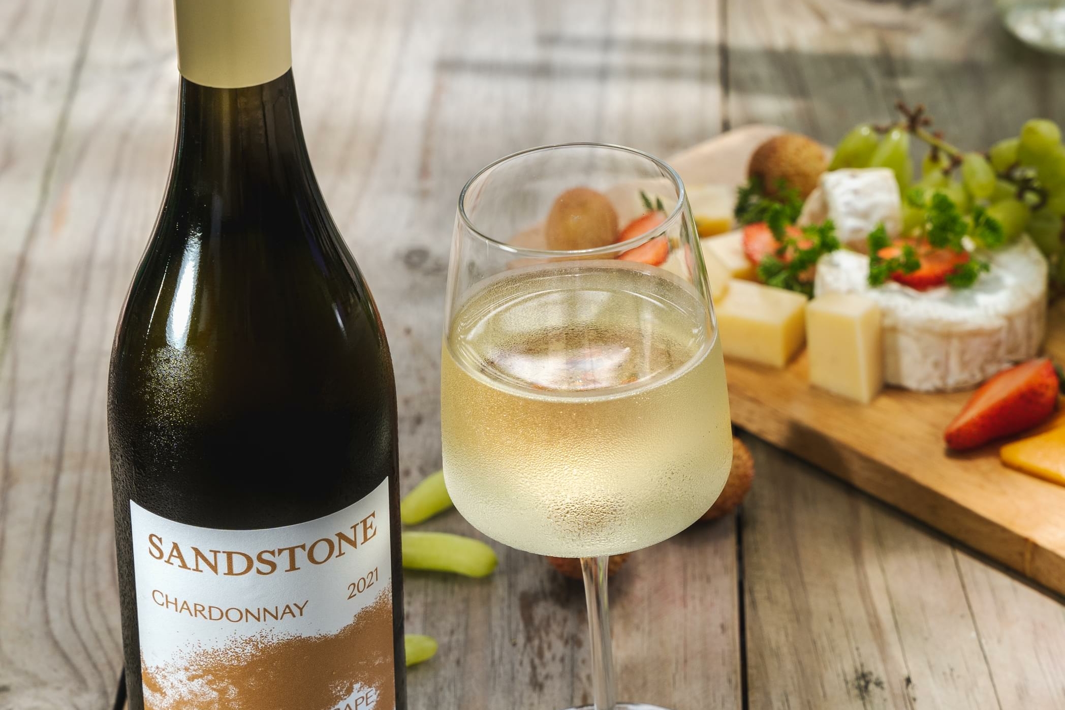 Bottle of Sandstone Chardonnay with a filled glass at Villa Resorts, set beside light dishes on a table