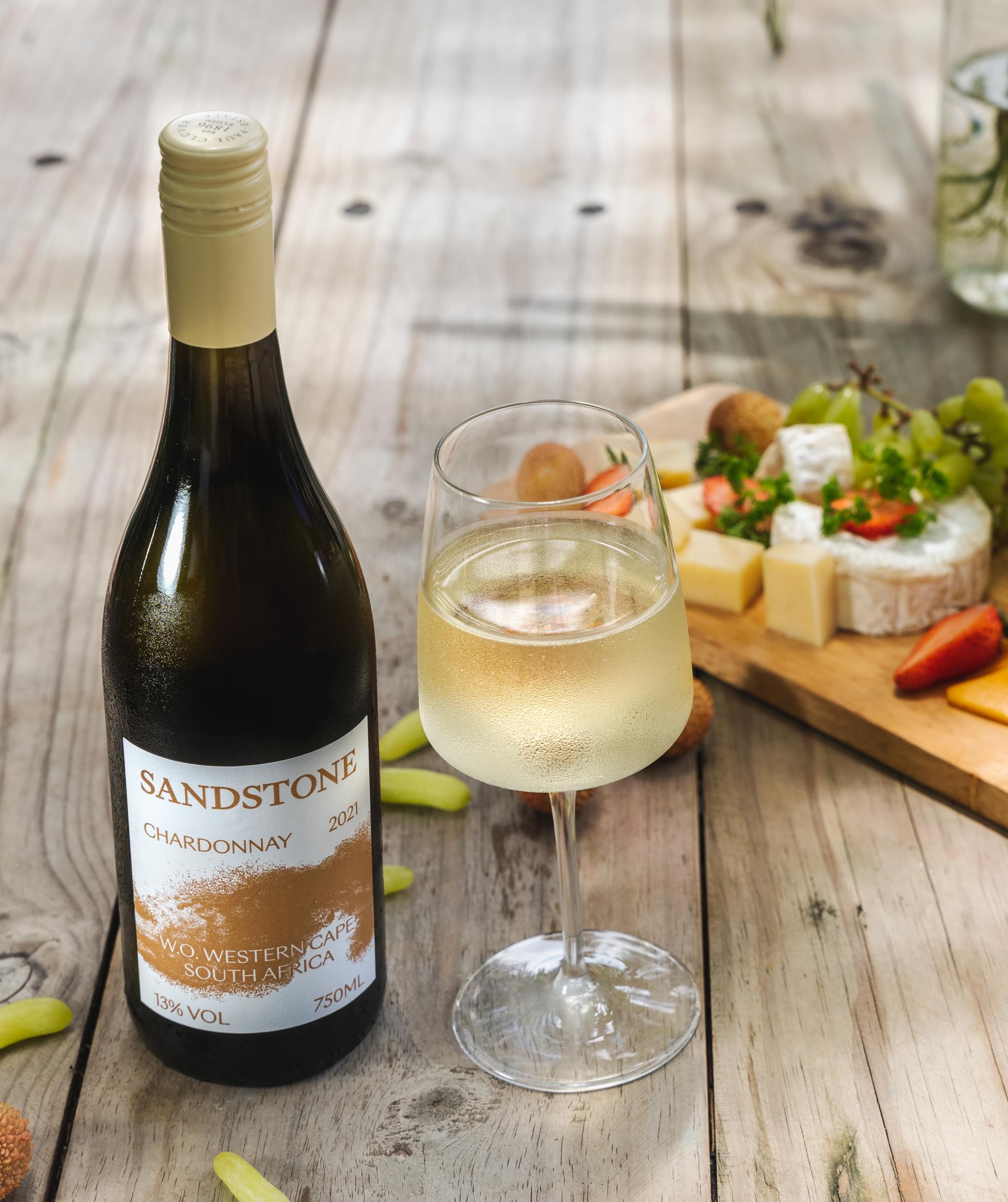 Bottle of Sandstone Chardonnay with a filled glass at Villa Resorts, set beside light dishes on a table
