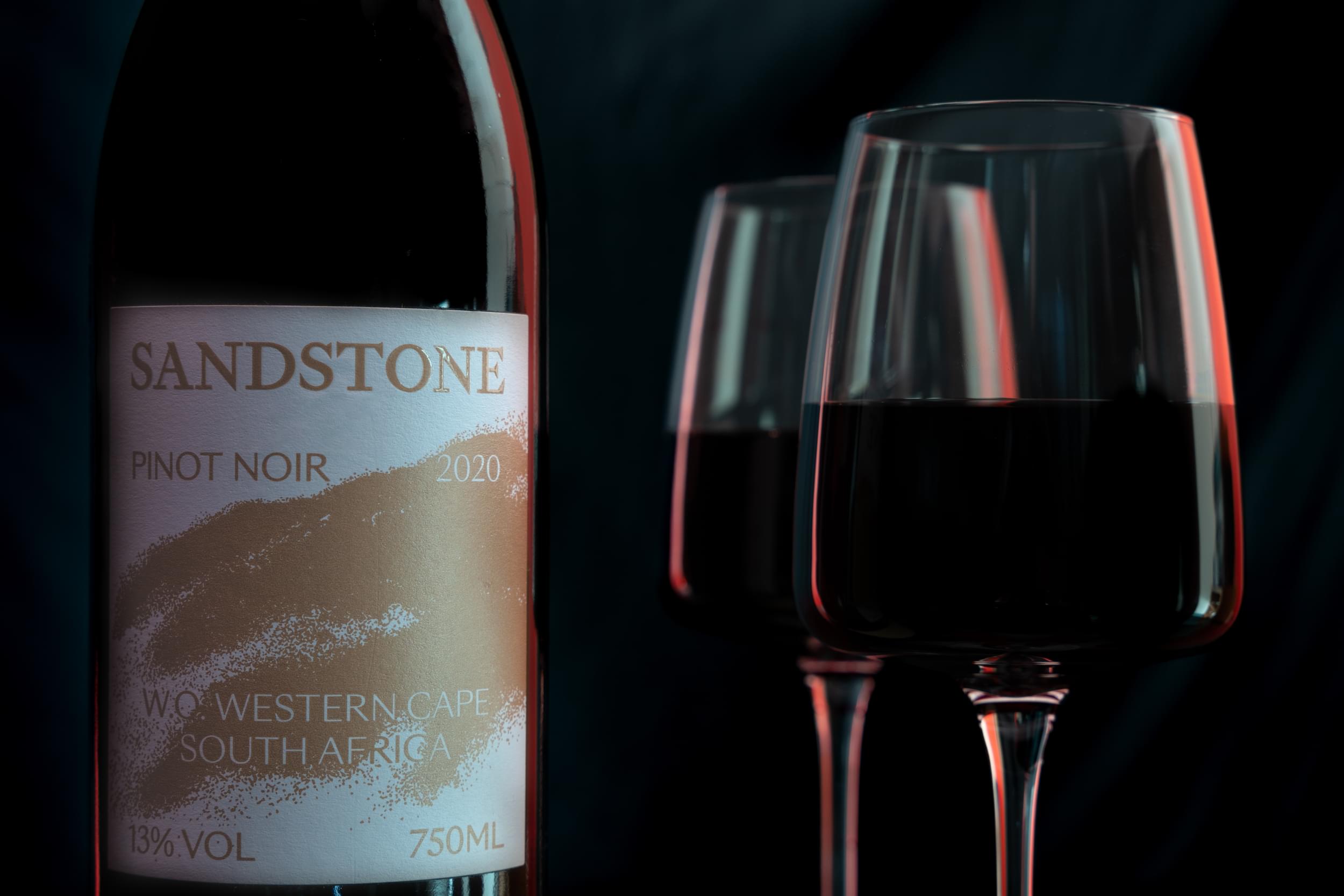 Close-up of Sandstone Pinot Noir with two red wine glasses at Villa Resorts against a dark background