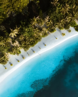 Aerial view of the beach at Villa Nautica with clear turquoise water, white sand and palm trees lining the shoreline