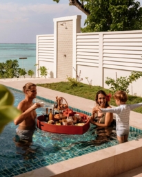 Family enjoying a floating breakfast in a private pool at Villa Park, with ocean views beyond the villa
