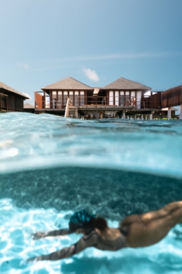 Snorkeller swimming beneath overwater villas in the clear lagoon at Villa Nautica Maldives